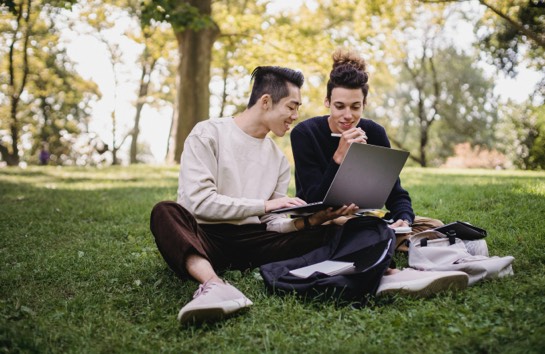 Two students on a computer outside on the lawn