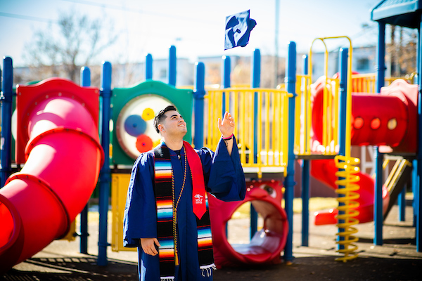 Student throwing graduation cap in front of a playground