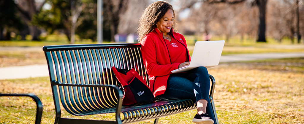 Woman in MSU Denver clothing sitting on a bench with her computer