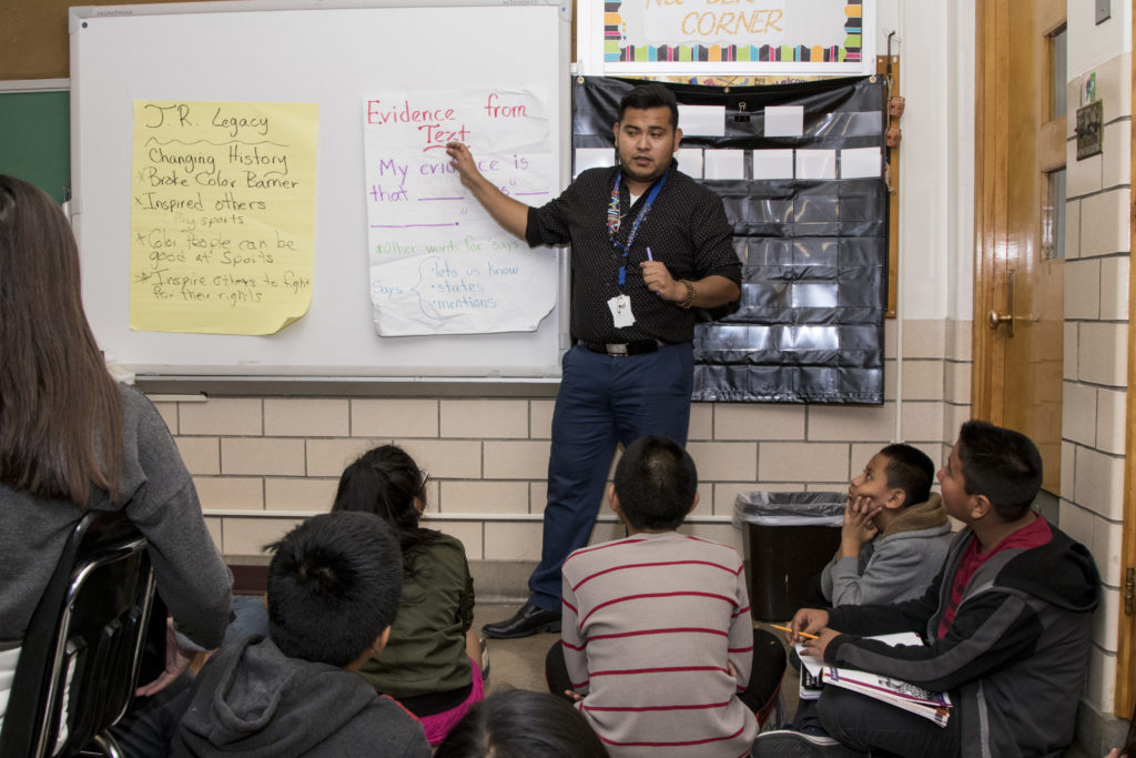 Elementary school teacher Hazael Roman Lagunas standing at the front of the class with students sitting on the floor in front of him.