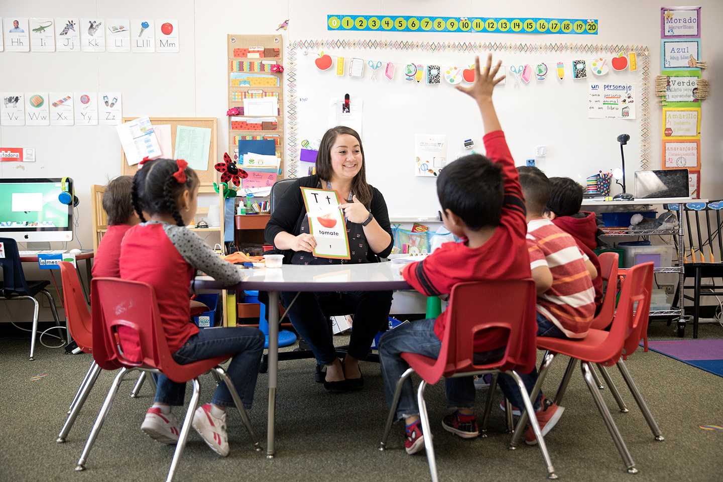 Elementary teacher Jacqueline Lujan sitting at a table in a classroom with children