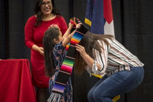 A little girl putting the latinx stole on her mom.