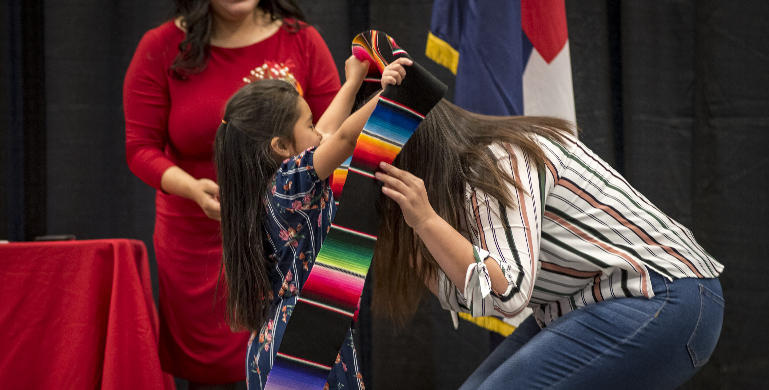 A little girl putting the latinx stole on her mom.