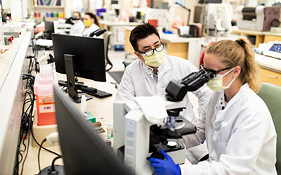 Students looking in a microscope in lab during their clinical rotation.