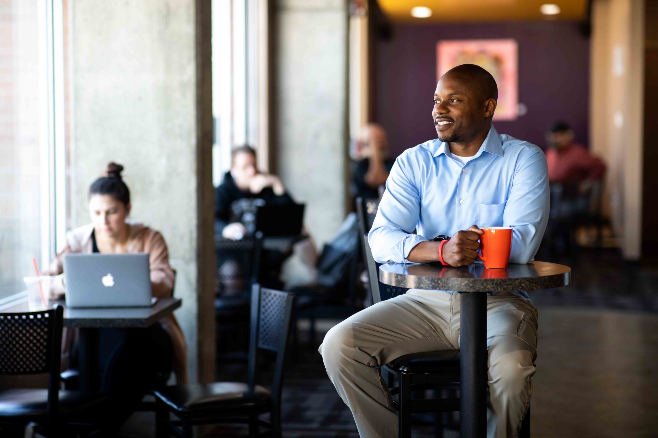 MSU Denver Grad Ryan Cobbins sitting in a coffee shop with a mug in his hand, looking out the window.