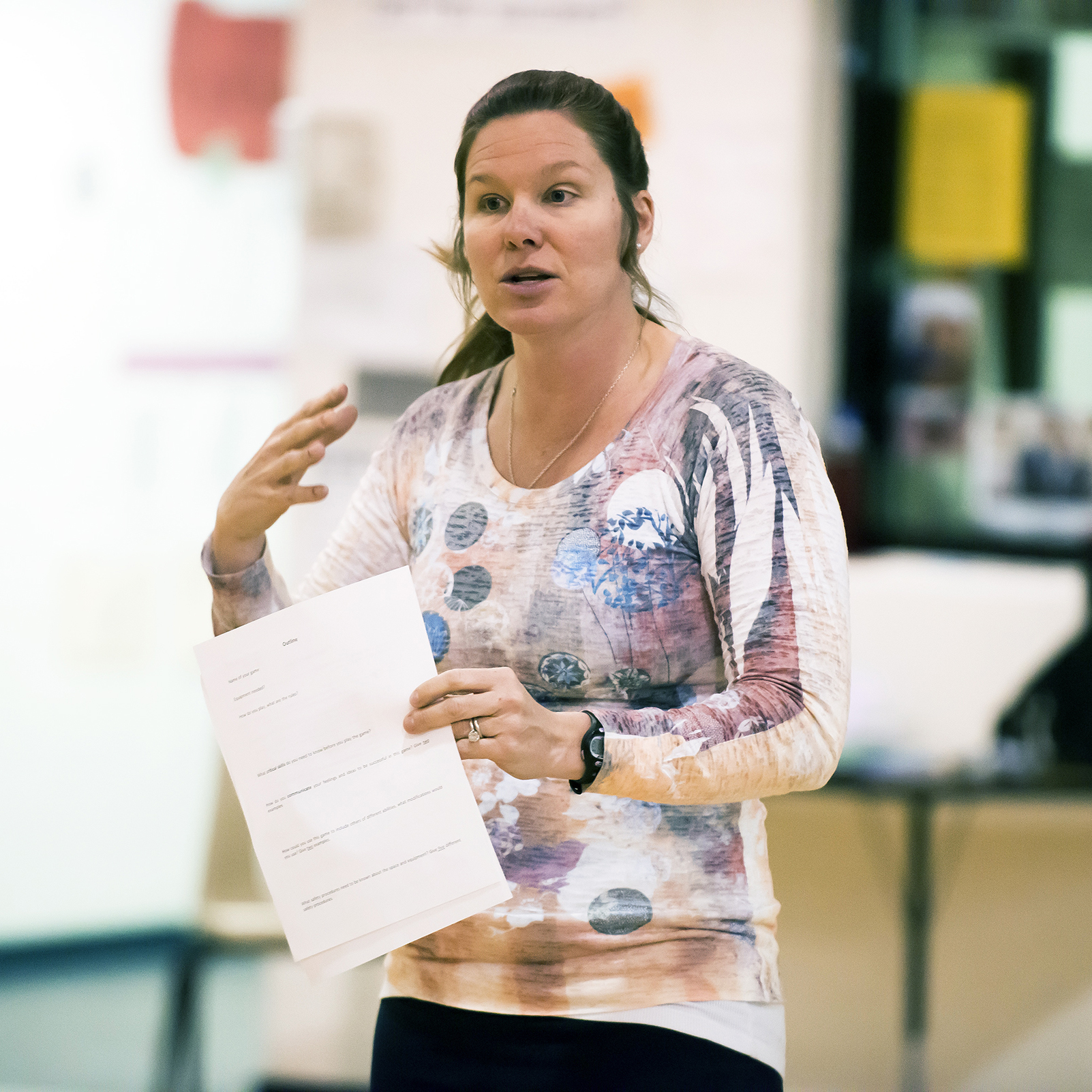 Decorative: Image of Elizabeth Minor teaching. She stands and gestures with one hand and holds papers with another.