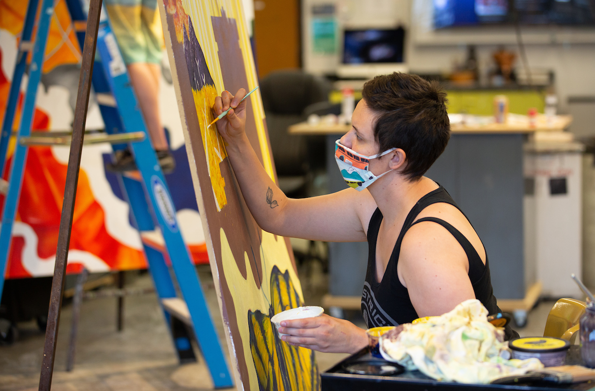 An art student wears a face covering while painting a class project.