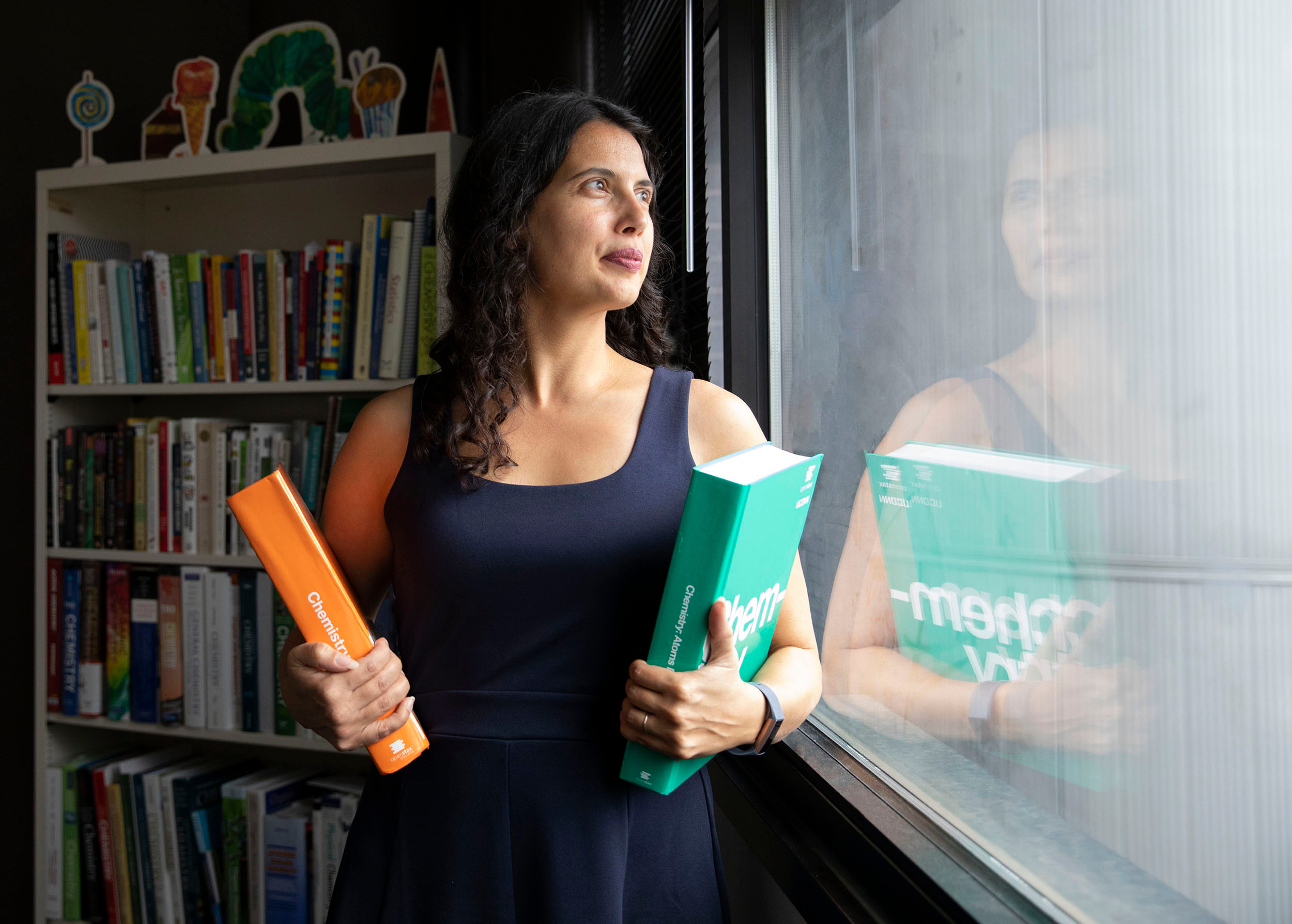 Emily Ragan looking out a window holding two books in each arm