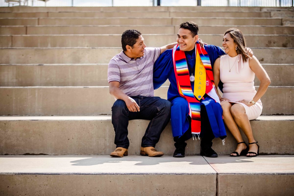 A graduate sitting on a set of stairs with their family