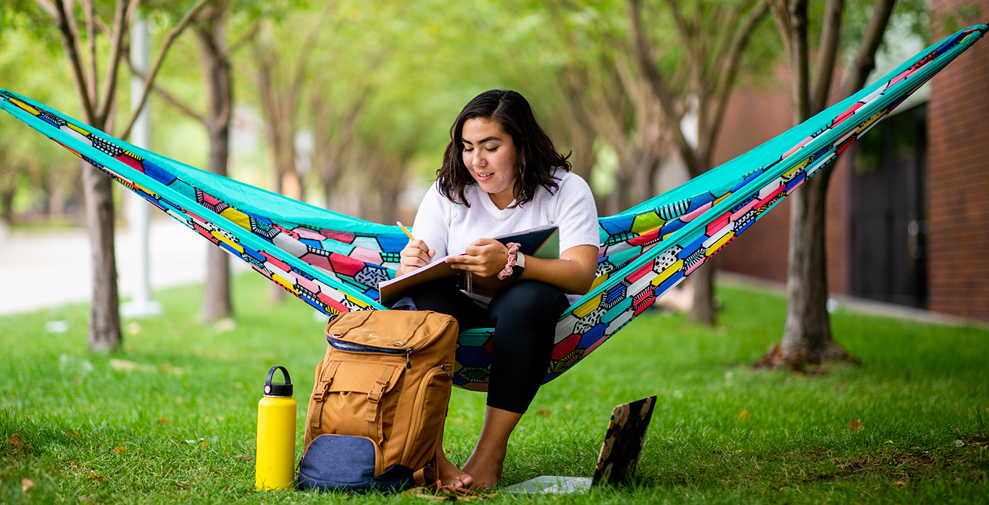 A student studying on a hammock outdoors.