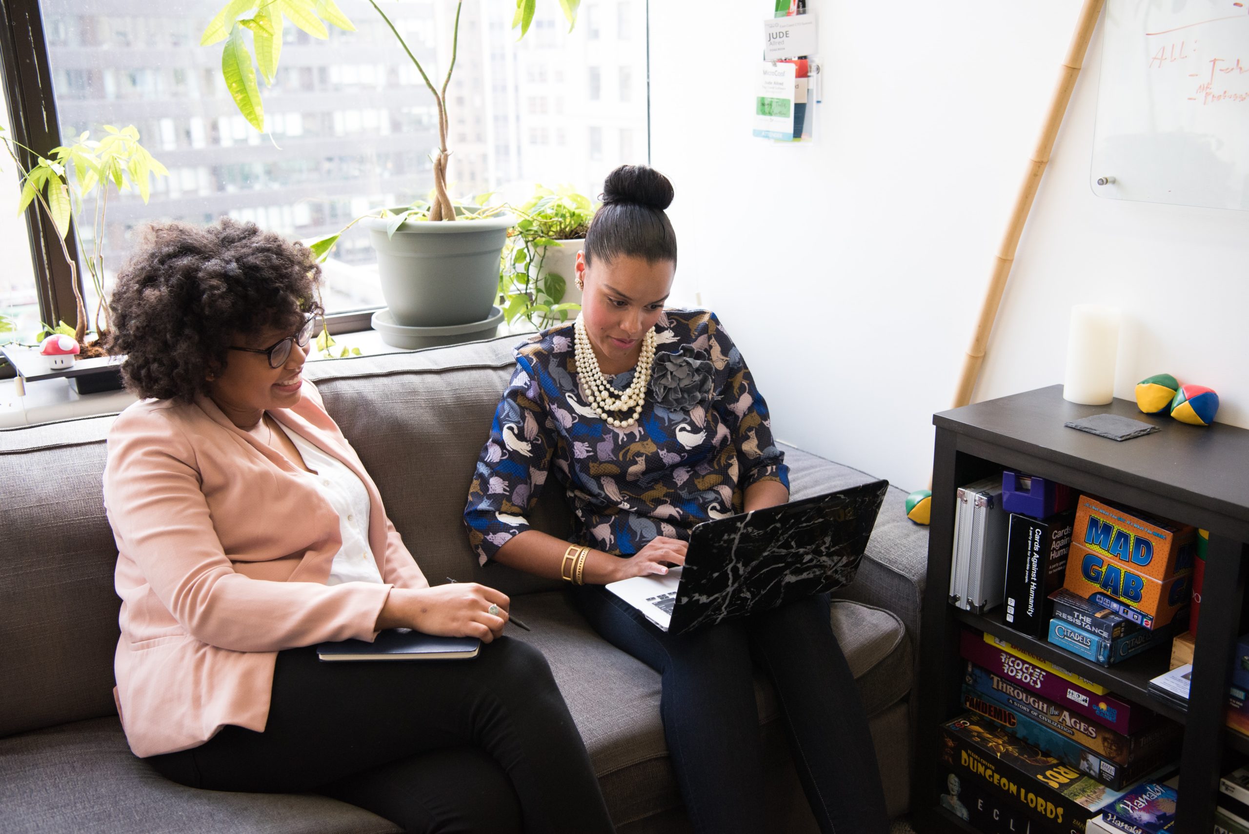 Two women sitting on a couch together looking at a laptop