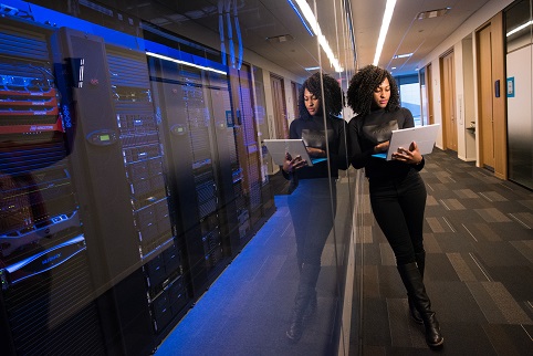 Woman next to servers holding and looking at laptop