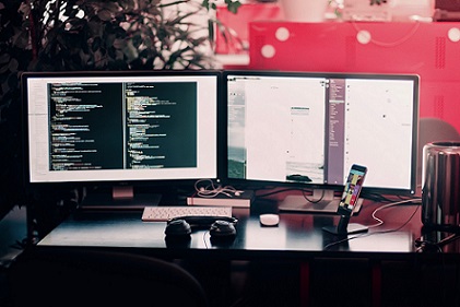 Two computer monitors, at office desk, displaying programming code