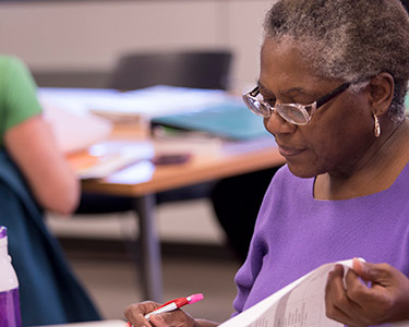 Adult student with pen in hand reading a workbook in class.