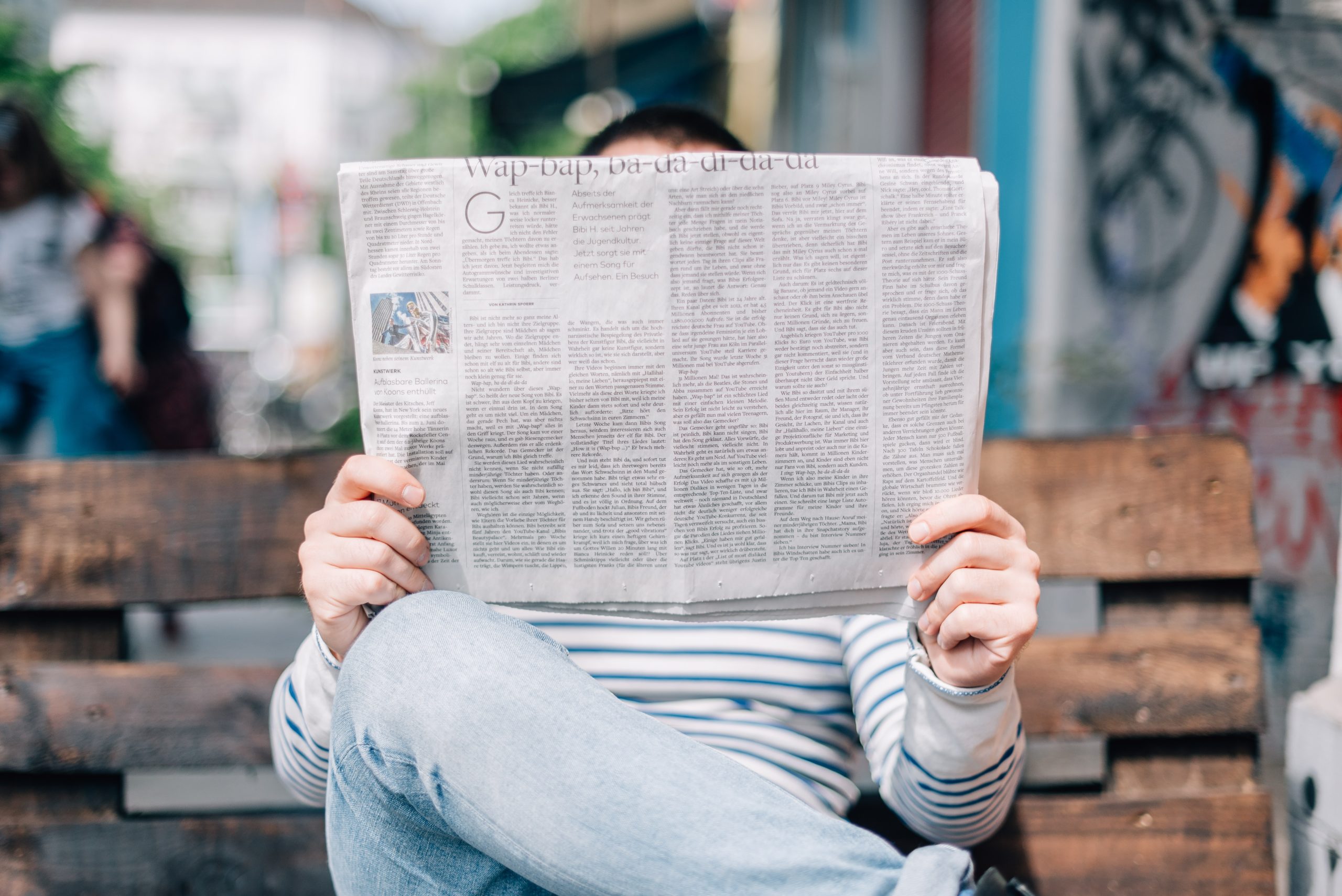 A Person sitting on bench reading a newspaper