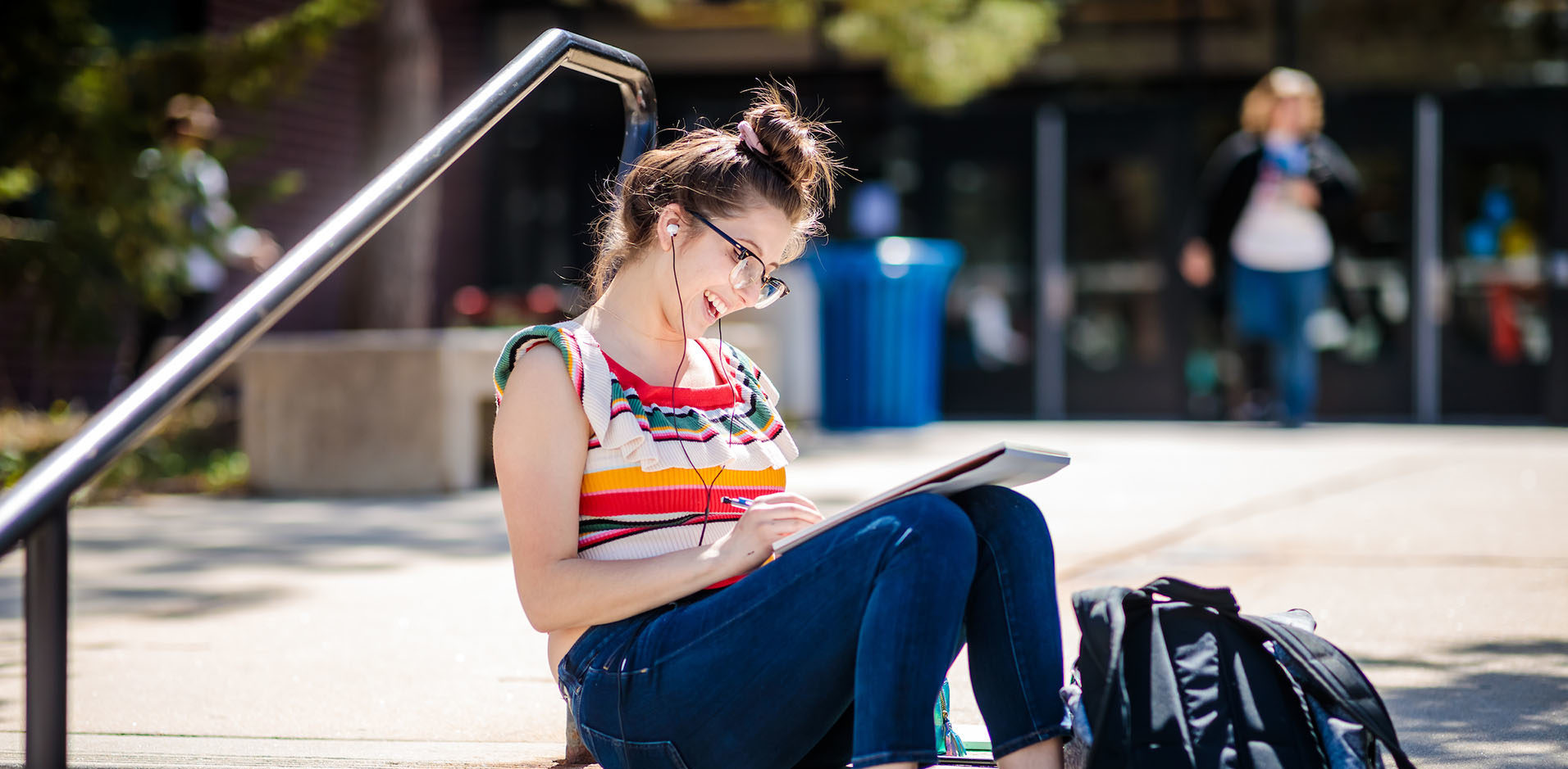 Student sitting on stairs writing in notebook and with headphones