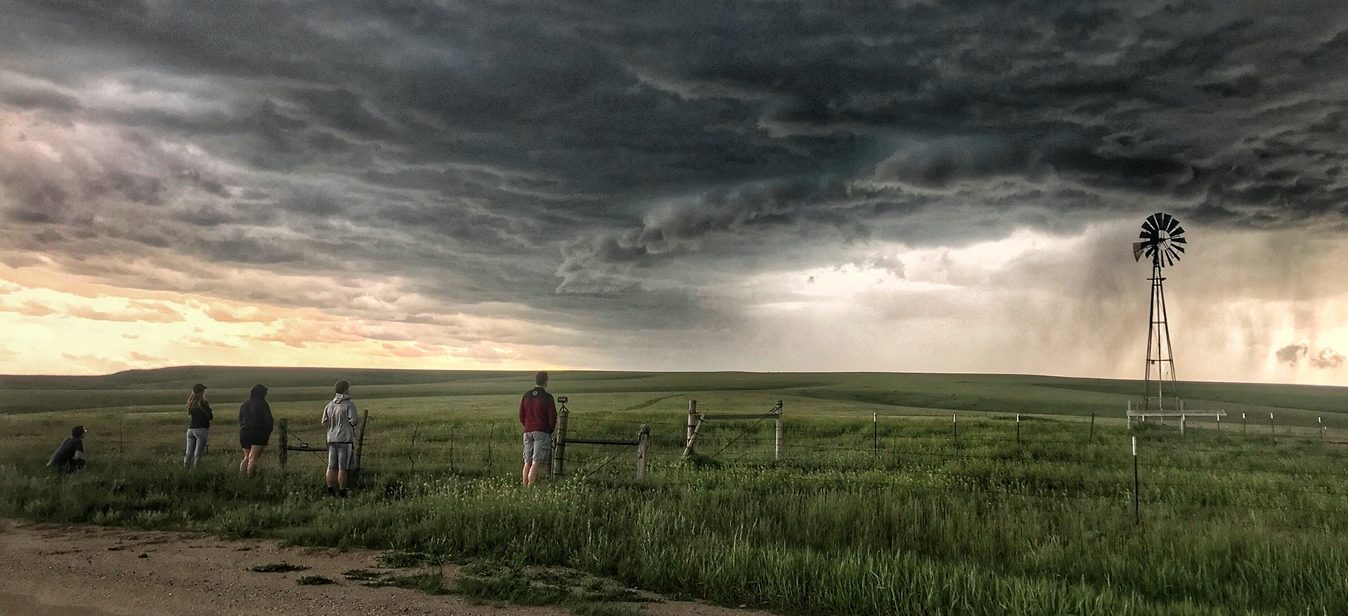 Students in a field with a windmill observing storms over the plains