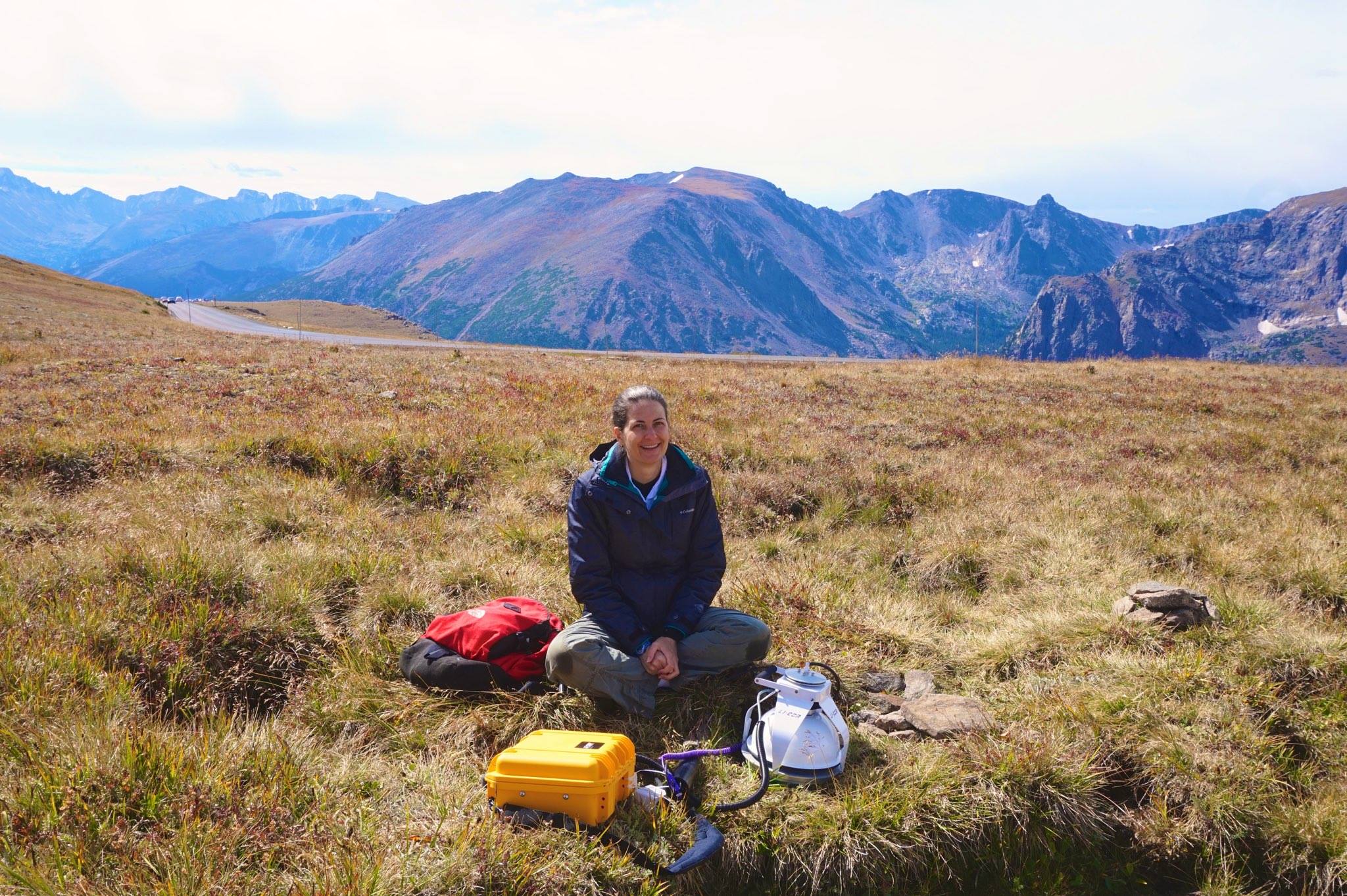 Professor Sarah Schliemann sitting in a high elevation field with mountains behind her.