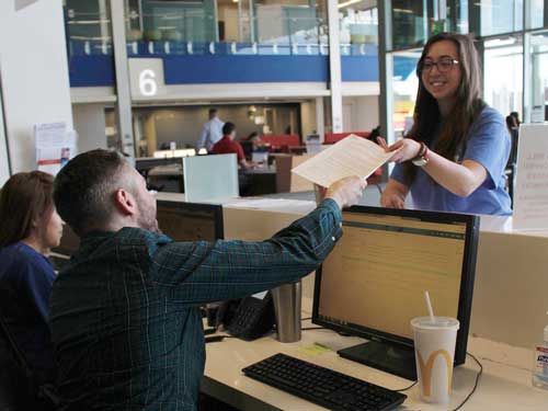 A MSU Denver student handing a piece of paper to a worker behind a counter