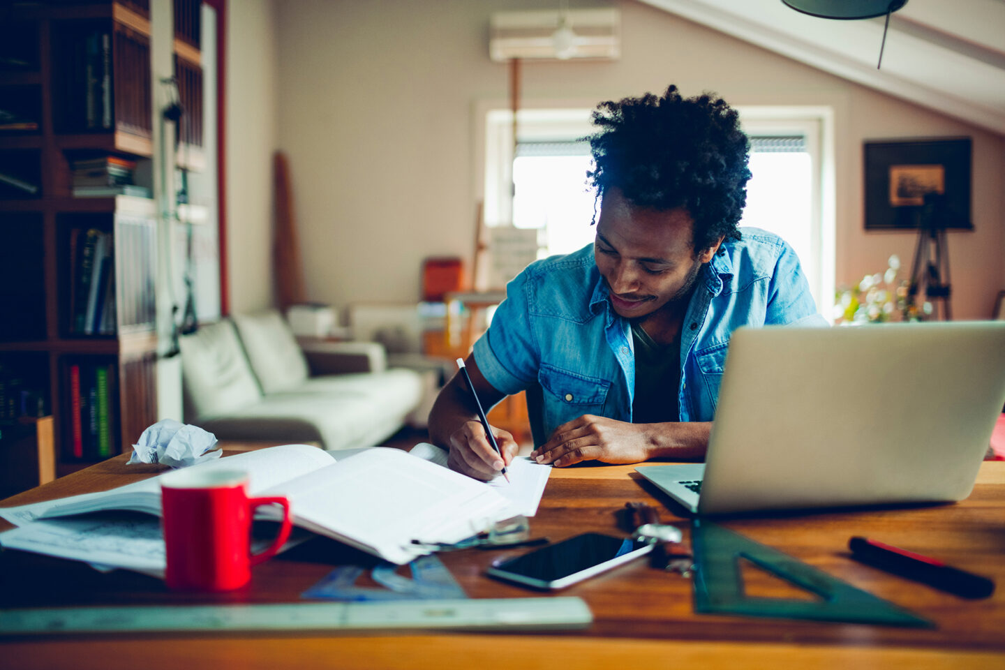 Man writing on paper in front of computer in his home
