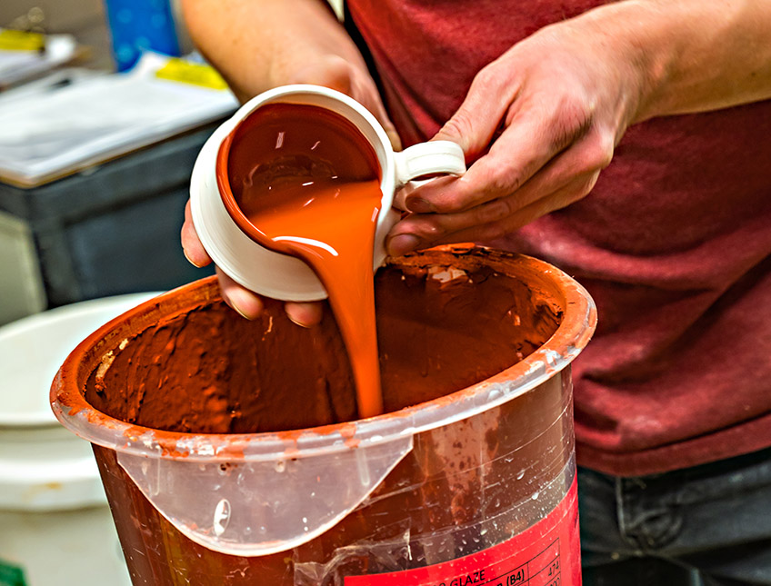 Pouring orange glaze out of a mug for pottery