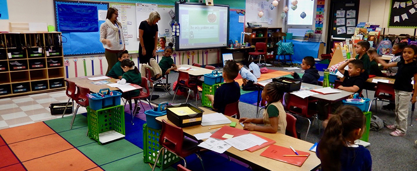 Photograph of two teachers instructing children in a classroom.