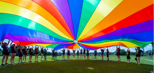 Students standing under a rainbow colored fabric lit by the sun