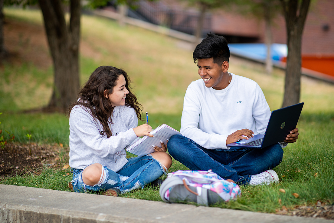 Students sitting outside studying and smiling