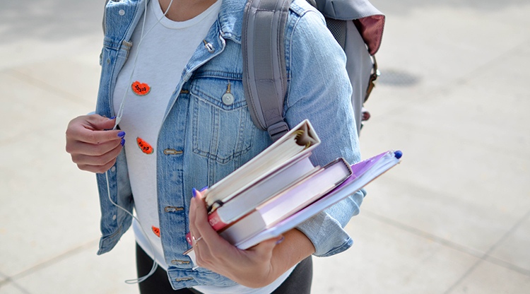 Student wearing a backpack and holding books and binders