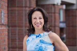 Maria Hinojosa in front of a brick building wearing a light blue shirt.