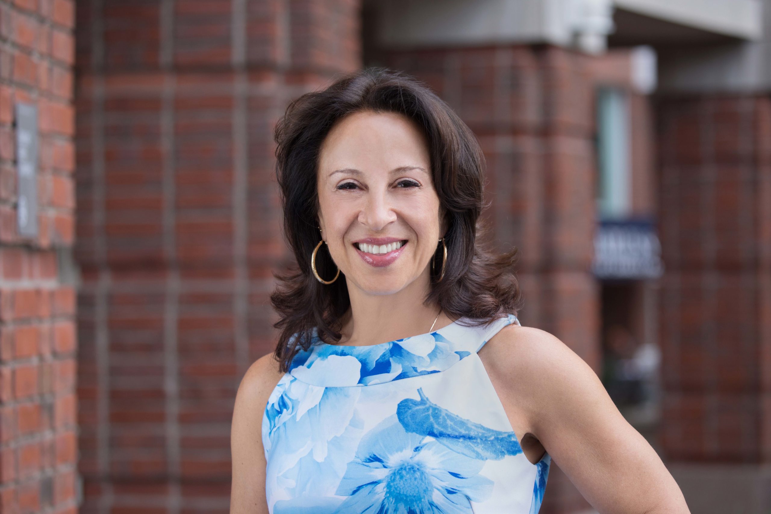 Maria Hinojosa in front of a brick building wearing a light blue shirt.