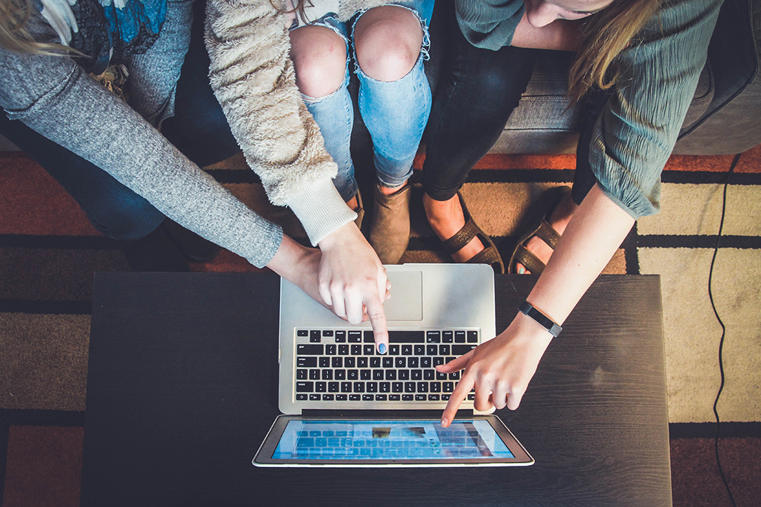 Group of students gathered around a laptop, pointing at the screen