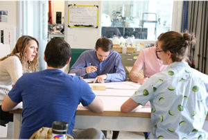 Industrial Design students talking and sketching around a lab table.