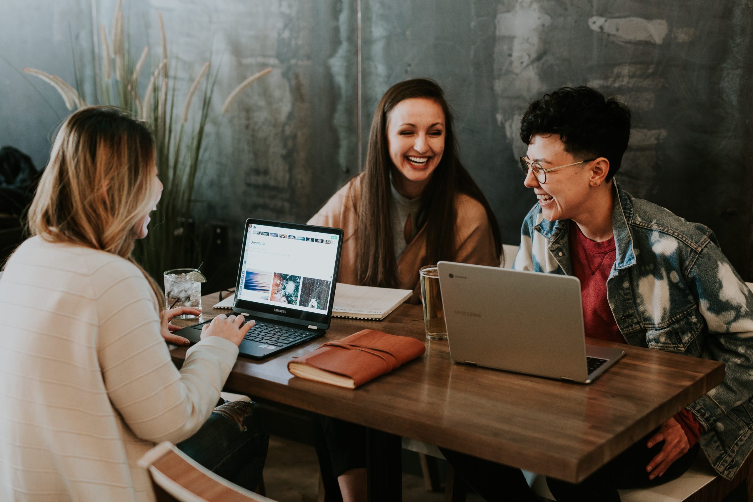 Three people laughing and sitting at a table with their laptops