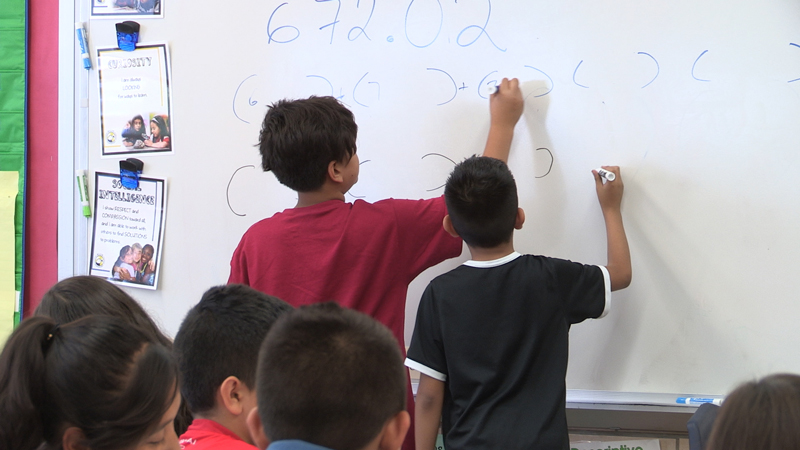 Image of two elementary school boys standing at the white board solving a math equation.