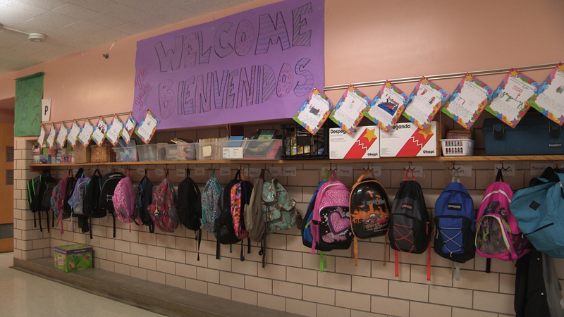Image of backpacks hanging from hooks in the hallway of an elementary school.