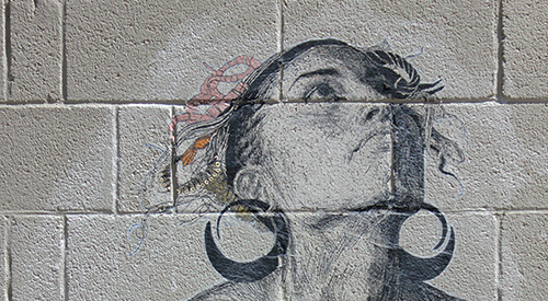 A concrete block wall with an image wheat pasted to it of a woman looking towards the sky