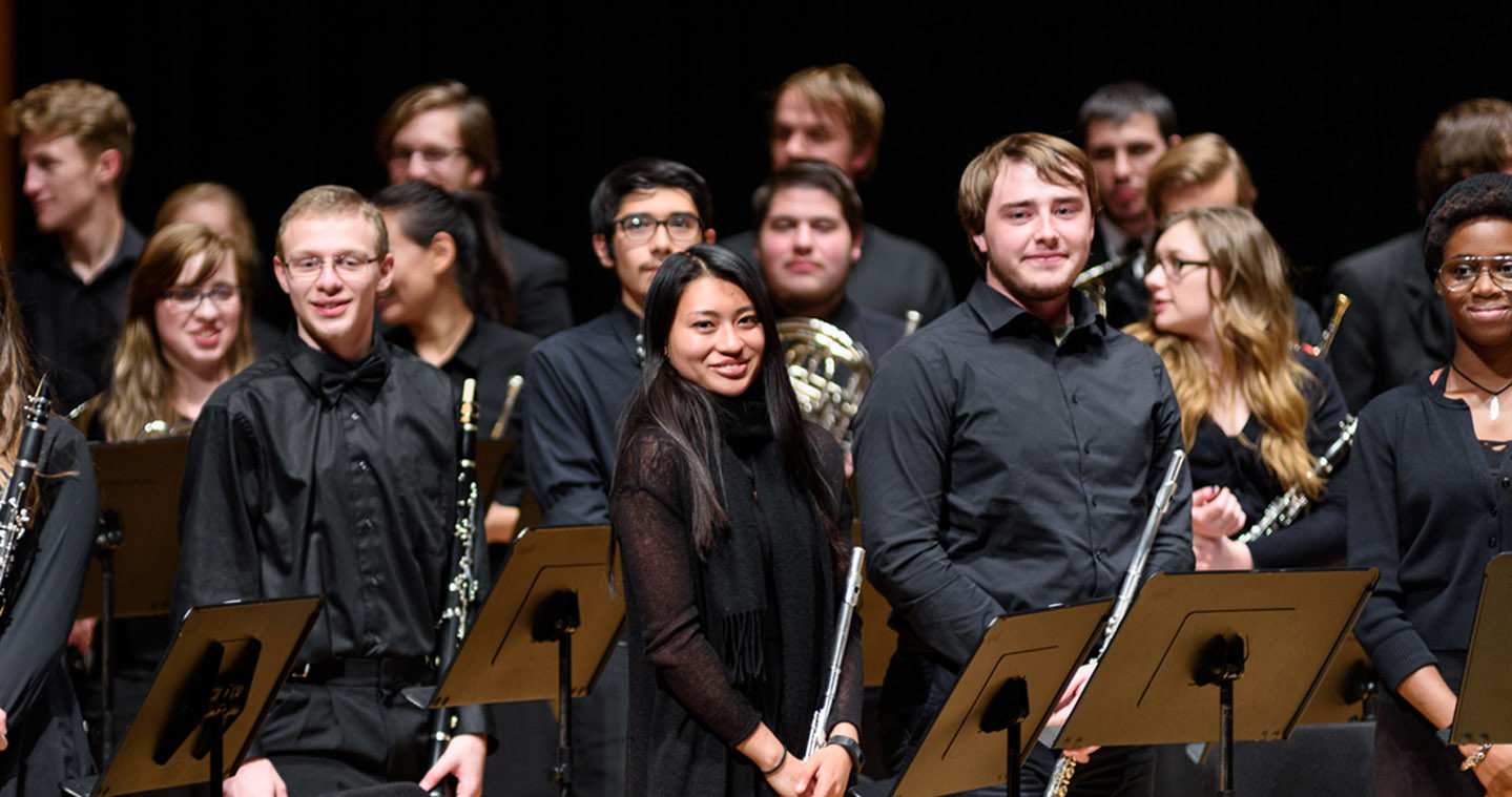 Flute section of a symphonic band standing and smiling after a performance