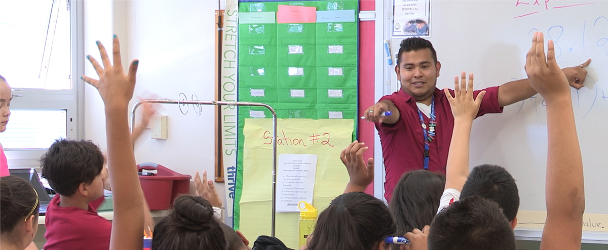 Teacher in an elementary classroom pointing to a student with their hand raised.