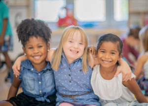 Image of three children sitting together smiling for the camera.