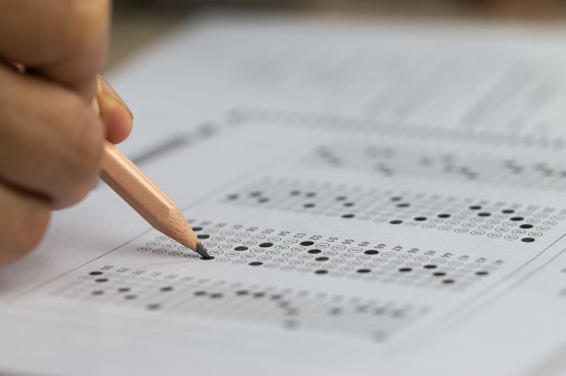 A hand holding a pencil filling in an exam bubble answer sheet