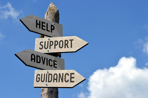 Wooden singpost with “help, support, advice, guidance” arrows against blue sky.