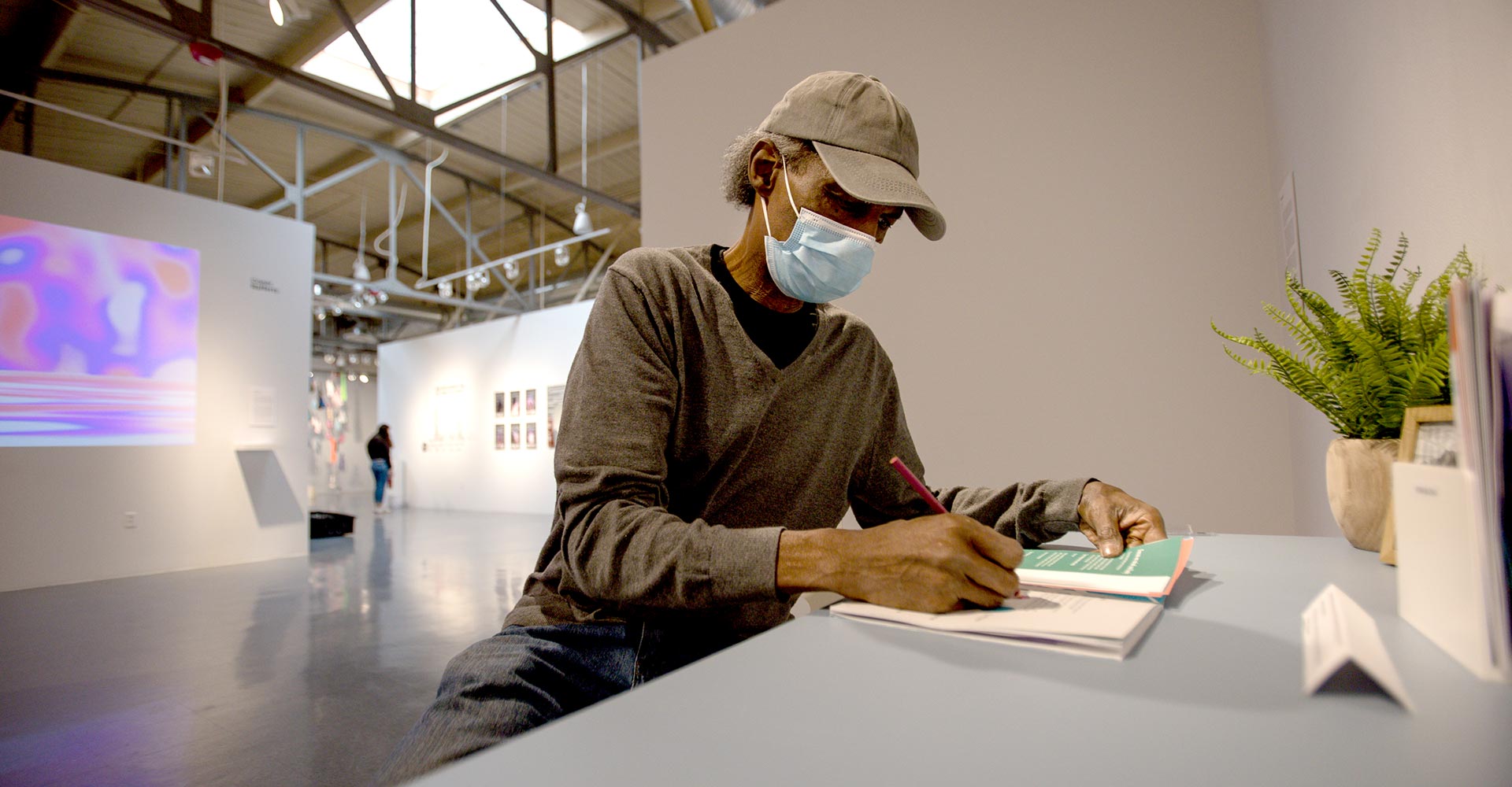 Travis Broxton in a mask seated reading a book on a table
