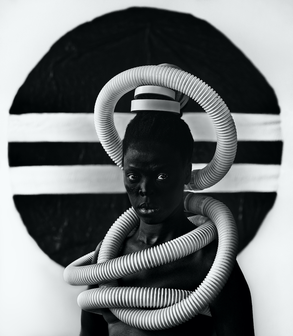 A person wrapped in vacuum tubing against a circular striped background.
