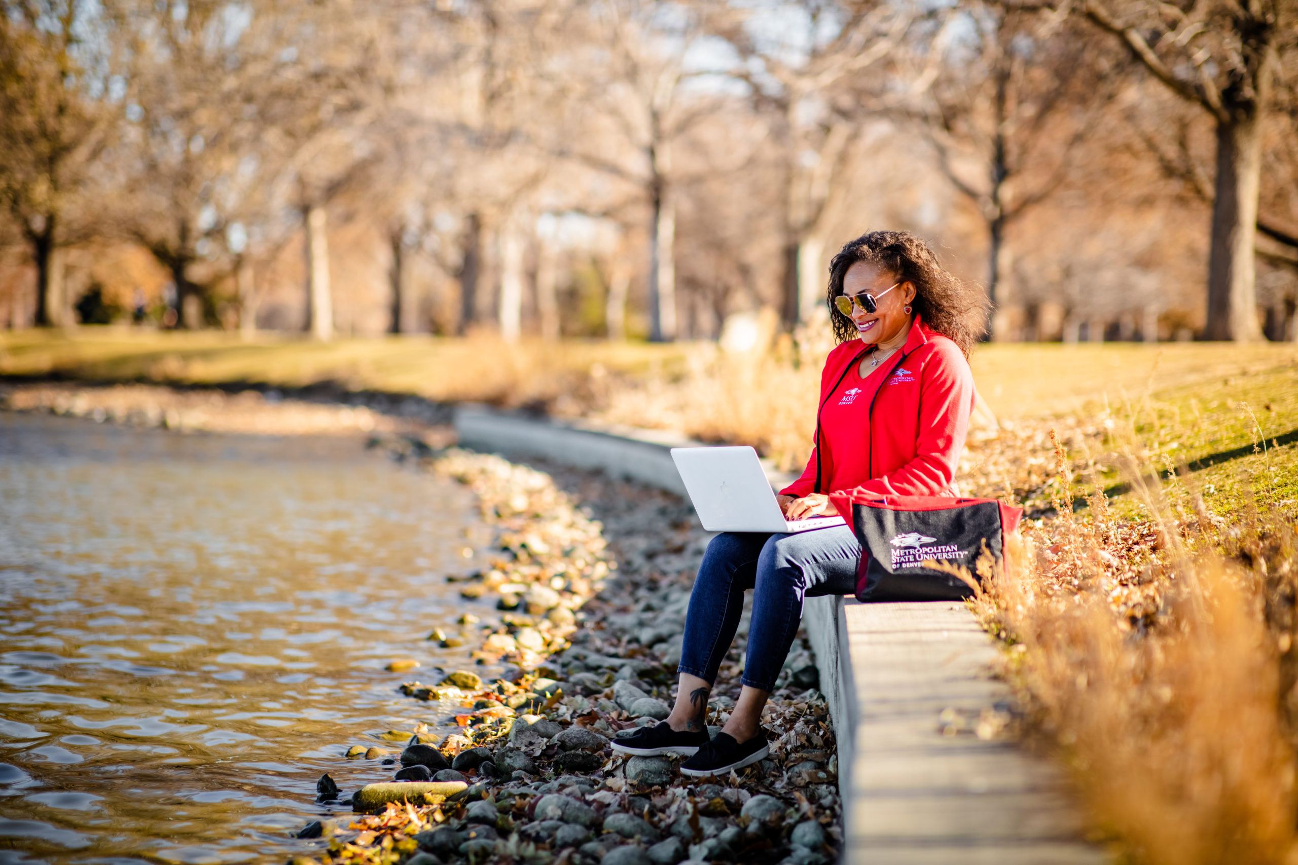 A student sitting on a concrete seat outside typing on their laptop