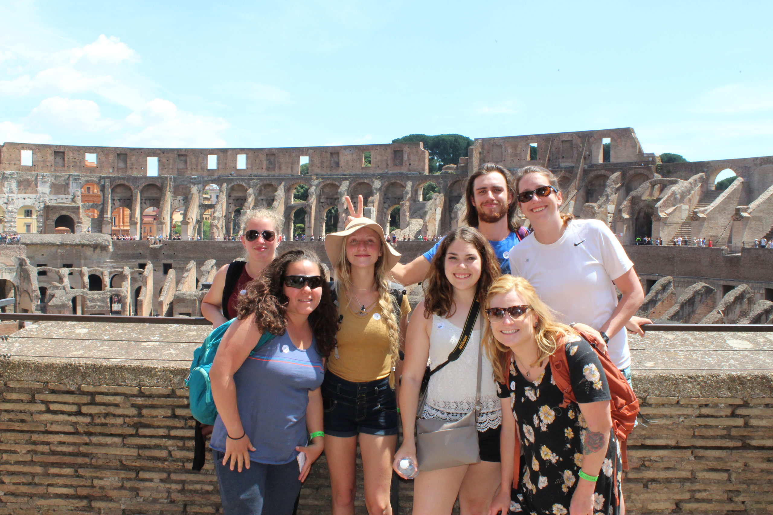 six women and one man posing in front of the colosseum in rome, italy