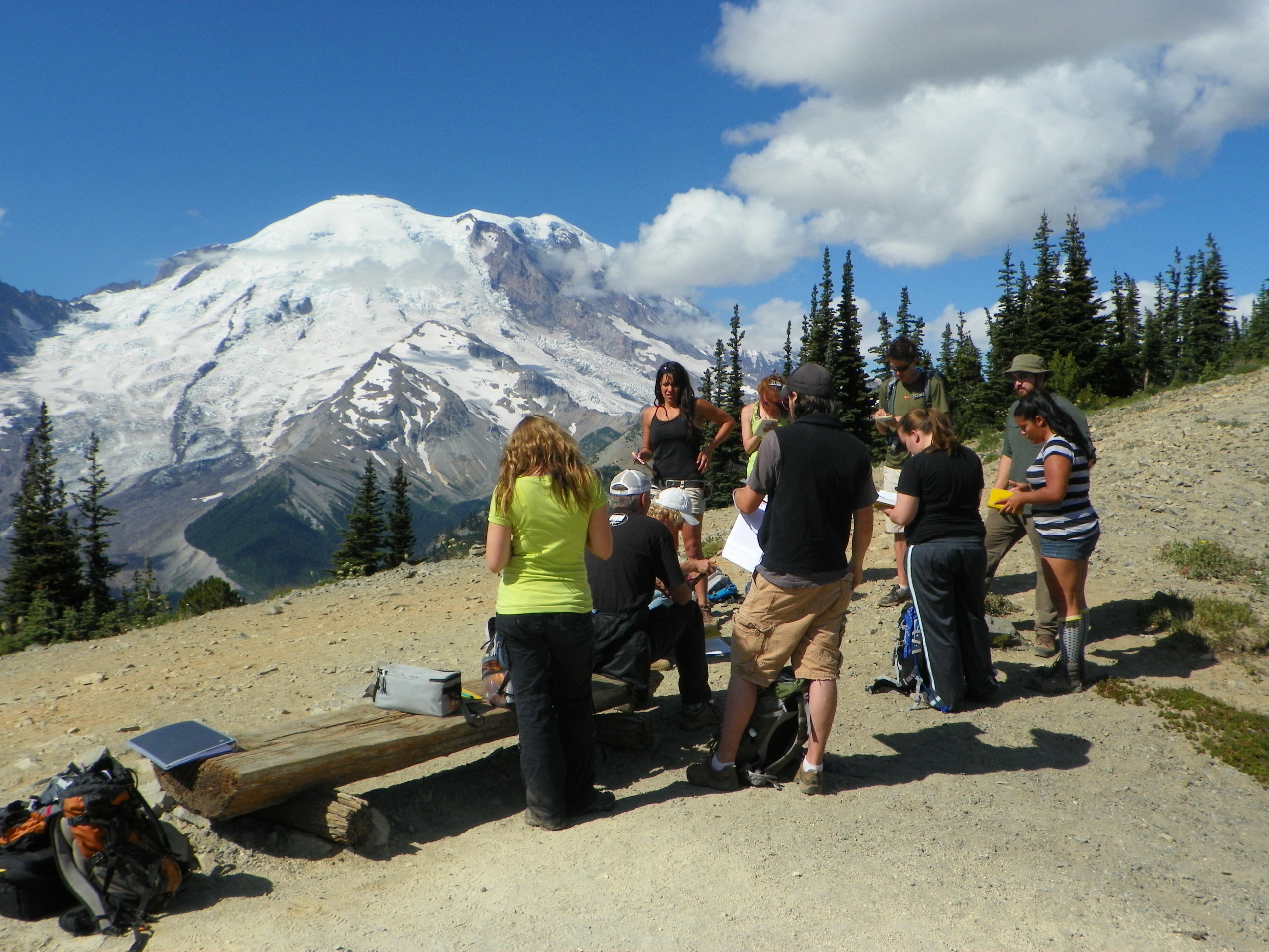 students huddled around an instructor with a snow capped mountain in the distance