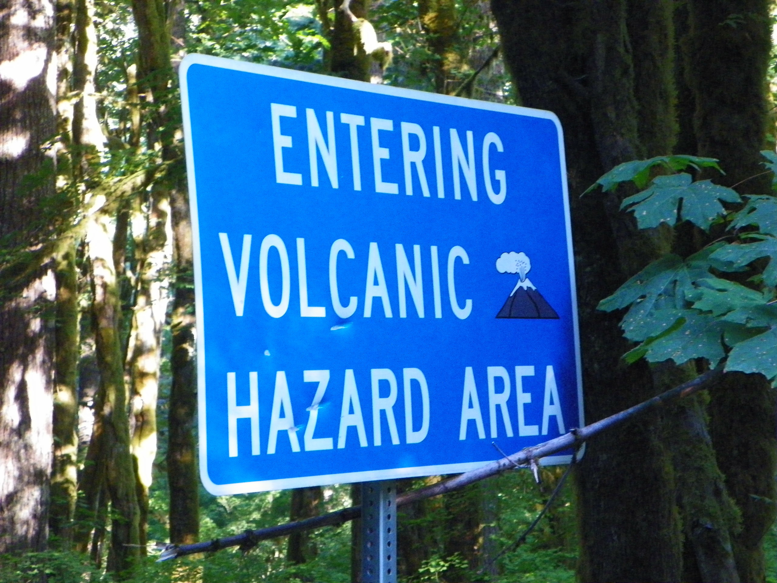 blue sign with a smoking volcano cartoon with the text entering volcanic hazard area