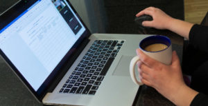 A close up of a woman holding coffee while working on her laptop.