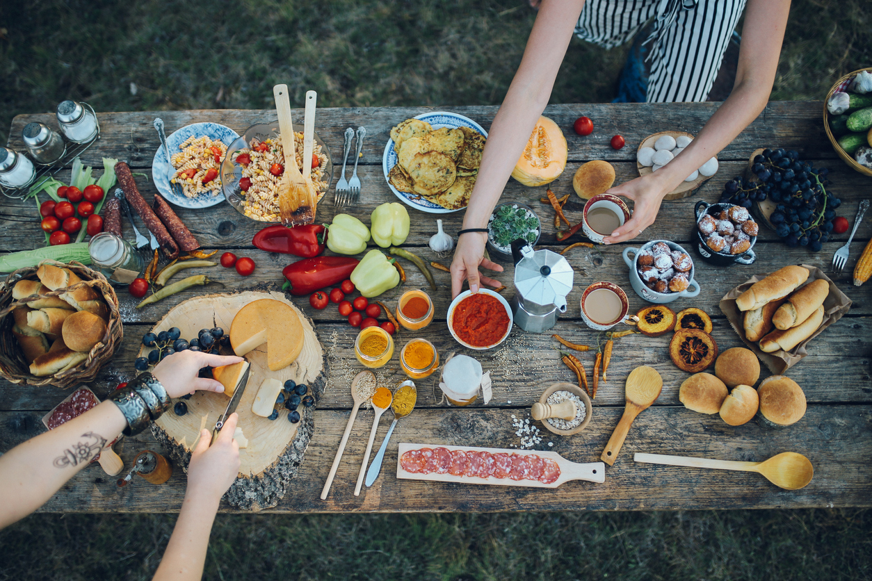 Overhead view of wooden table full of food with people's arms passing food
